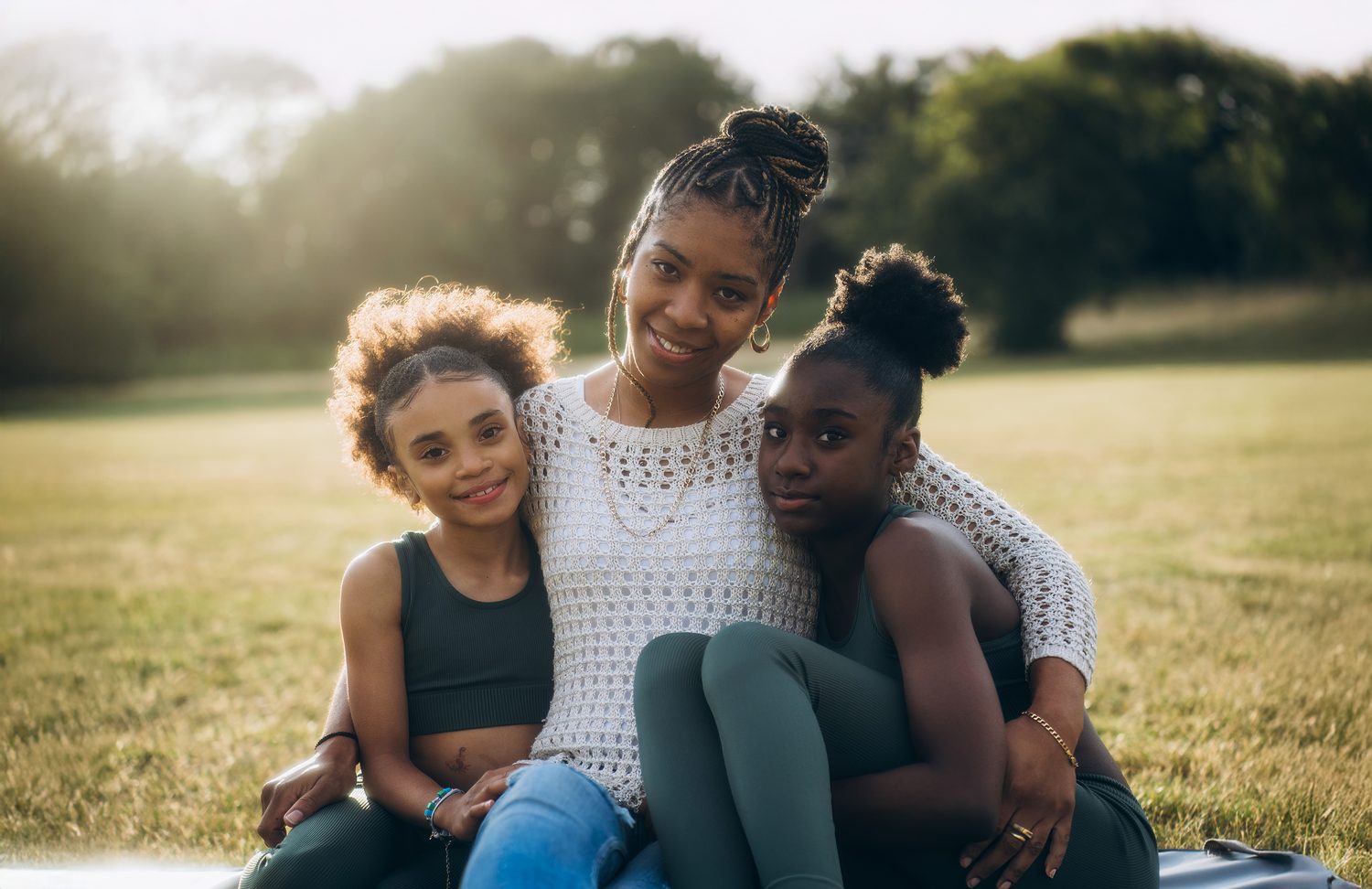 Mother cuddling her two daughters on the grass in late golden sunlight on a family photoshoot