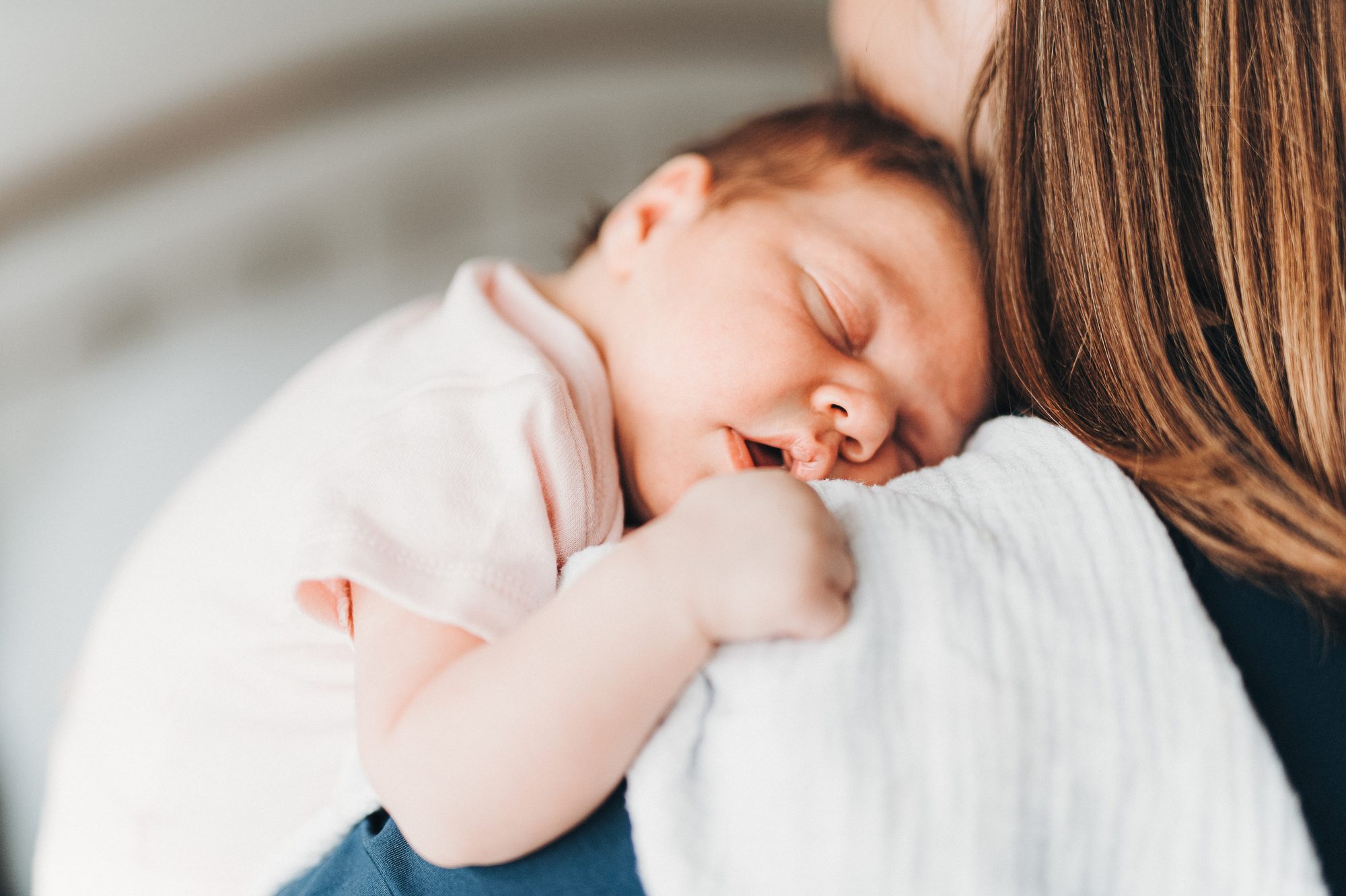 Newborn baby asleep on her mother's shoulder, wrapped in a white muslin