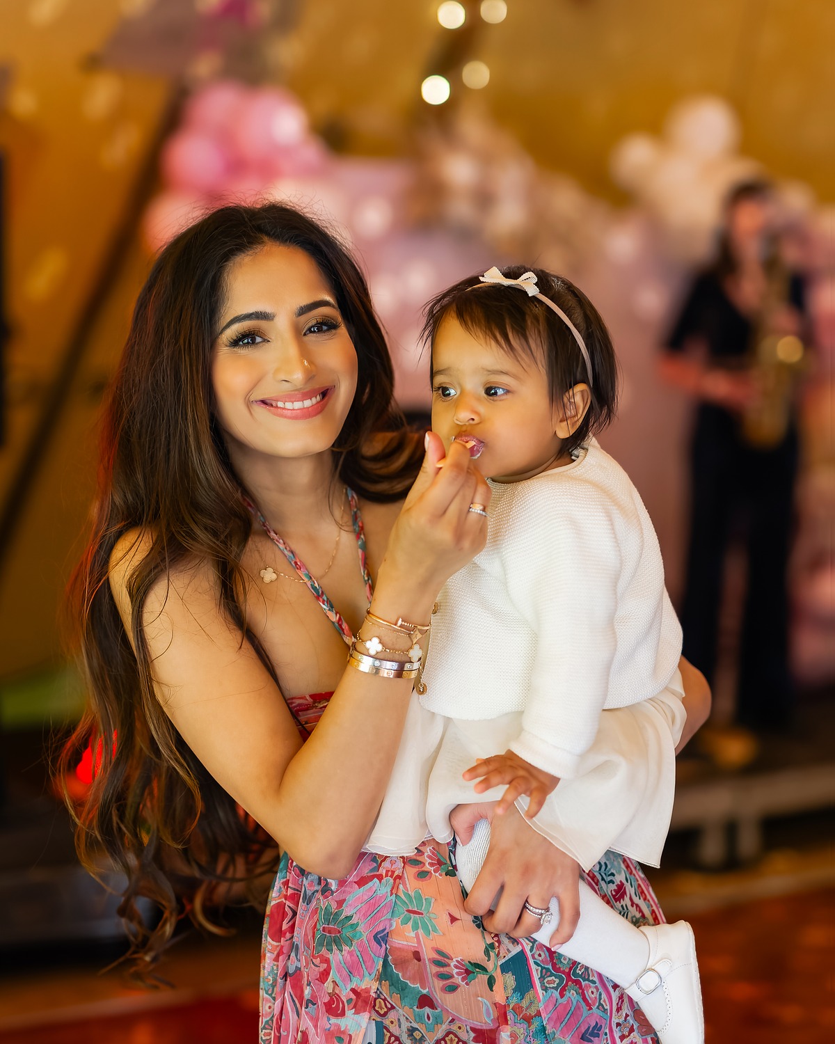 Mother smiling with her baby in her arms at a family celebration, a saxophonist playing behind them